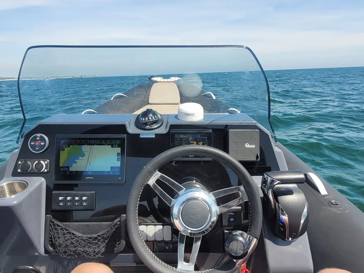 Le poste de pilotage en mer : volant, écran de navigation et pare-brise, la côte à l’horizon