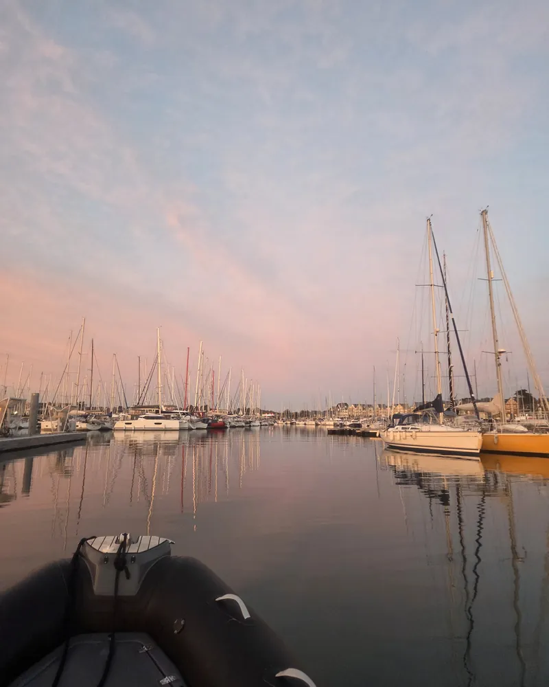 Retour au port à la tombée du jour : l’avant du semi-rigide, des voiliers au ponton, le ciel rose