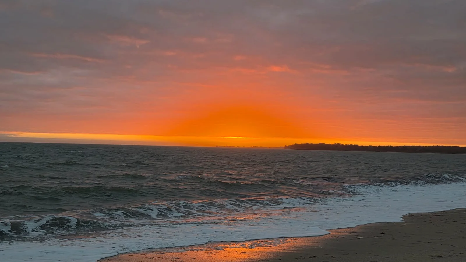 Le soleil vient de se coucher sur la mer à Landrezac, ciel rose et orangé et une vague sur le sable