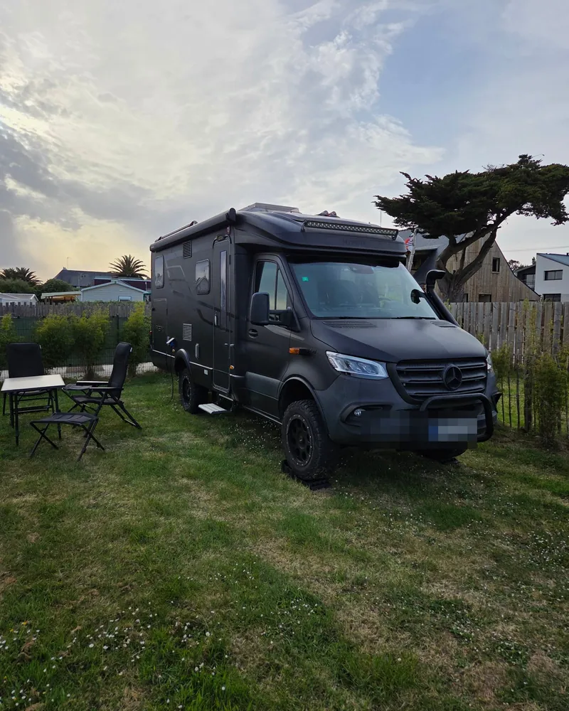 Un camping-car noir tout-terrain sur un emplacement en herbe, entre les arbres
