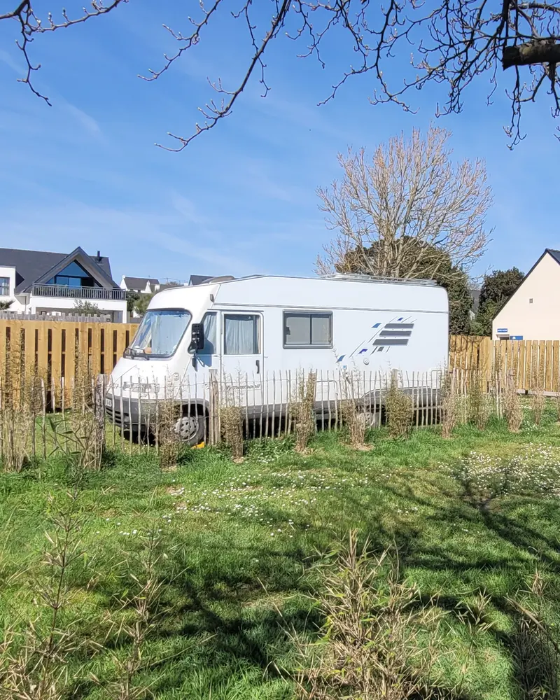 Un camping-car sur un emplacement en herbe, entouré de palissades en bois et d’une ganivelle