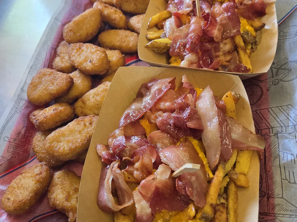Des nuggets de poulet et des frites garnies de bacon et de cheddar, servis en barquettes de carton à la guinguette
