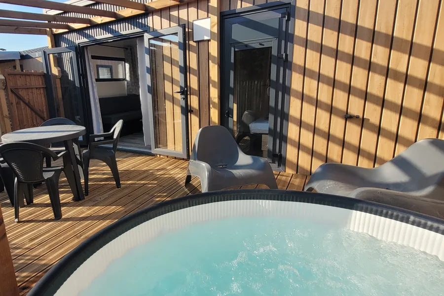 La terrasse en bois du mobil-home Bali sous sa pergola, avec le spa au premier plan, une table et des fauteuils