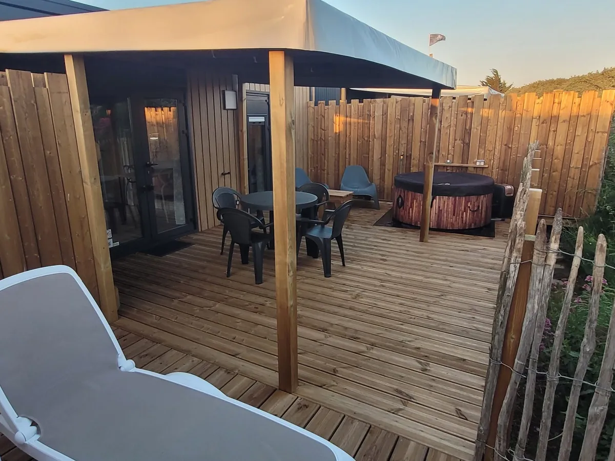 Le spa privatif sous son couvercle, sur la terrasse couverte d’un mobil-home, avec table, chaises, transats et ganivelle