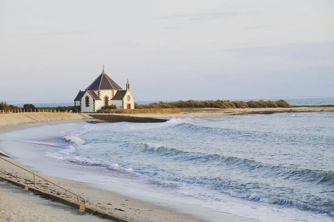 La chapelle Notre-Dame-de-la-Côte de Penvins, blanche sous un ciel clair, au-dessus de la plage de sable et des vagues