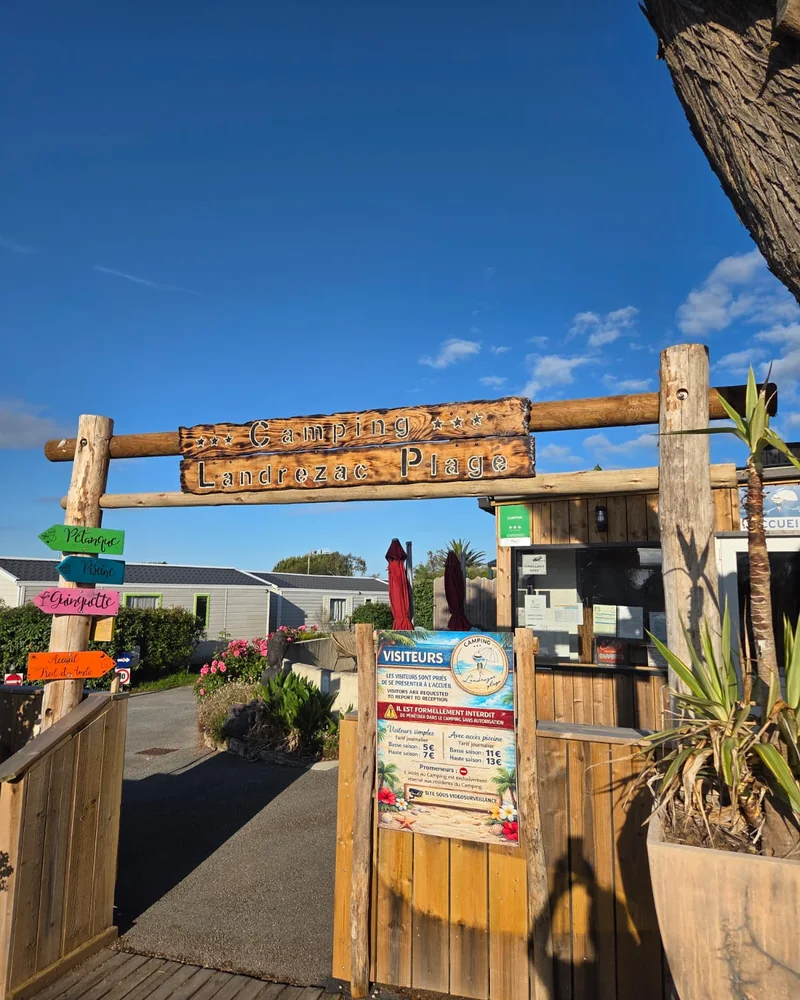 L’entrée du camping Landrezac Plage : l’enseigne en bois au-dessus du portail et le panneau indiquant la plage, la piscine, la guinguette et l’accueil