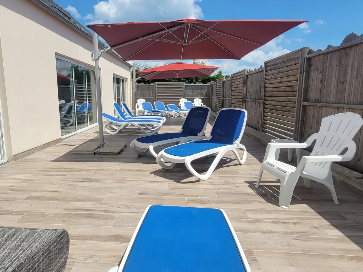 Le solarium de la piscine : transats bleus, fauteuils blancs et parasols rouges, à l’abri d’une palissade